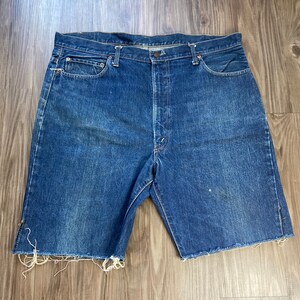 Puede incluir: Un par de pantalones cortos de mezclilla azul con bordes deshilachados. Los pantalones cortos tienen cierre de botón y cinco bolsillos.