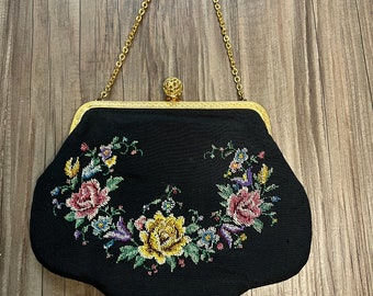 Könnte beinhalten: Eine schwarze Abendtasche mit einer goldenen Kettenkette und einem floralen Stickmuster. Die Stickerei zeigt rosa, gelbe und violette Blumen.