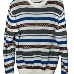 Puede incluir: Un suéter de cuello redondo a rayas horizontales en blanco, azul y gris, con una banda decorativa roja, amarilla y verde. El suéter tiene mangas largas y puños y dobladillo acanalados. La marca "Arrow" es visible en la etiqueta.