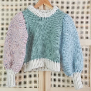 May include: A colorful knitted sweater with a green, blue, and pink color block design. The sweater has a white trim around the neck and cuffs.