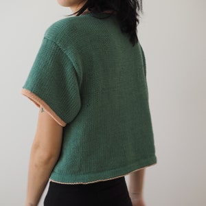 May include: A green short-sleeved knitted top with a peach trim around the neckline and sleeves.