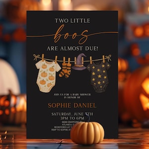 以下が含まれることがあります： 黒い背景に「Two Little Boos Are Almost Due!」というテキストが入った、ハロウィーンをテーマにしたベビーシャワーの招待状。招待状にはベビー服とかぼちゃが描かれています。背景には、ライトアップされたジャック・オー・ランタンと装飾ライトがあります。