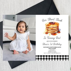 Puede incluir: Una invitación de cumpleaños con una foto de un bebé con un vestido blanco. La invitación incluye el texto "Our Short Stack Is Turning One!" y los detalles de la fiesta. Tiene un borde a cuadros blanco y negro. El fondo es de color neutro.