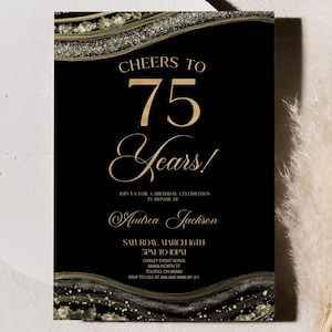 May include: Black and gold 75th birthday invitation. The invitation features the text "Cheers to 75 Years!" in gold script. The design includes gold glitter accents and a black background. The invitation is rectangular and is on a white surface.