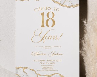 May include: A white invitation card with gold text and accents, celebrating an 18th birthday. The card reads "Cheers to 18 Years!" with the name "Andrea Jackson" and event details. A decorative pampas grass and a white circular object are in the background.