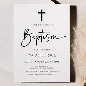 May include: A white baptism invitation card with black text and a cross graphic. The card includes the text "Please join us for the Baptism of our daughter Natalie Grace" and event details. A decorative pampas grass and a white circular object are in the background.