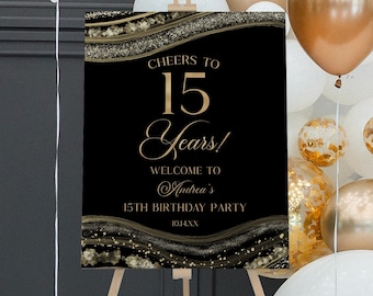 May include: A rectangular black welcome sign on a wooden easel featuring gold text that reads Cheers to 15 Years! Welcome to Andrea's 15th Birthday Party 10.14.XX. The sign has decorative gold and black glittery wave patterns at the top and bottom.