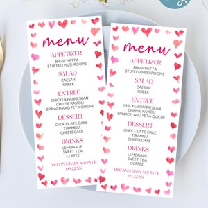 May include: Two pink and white printable menu cards with a watercolor heart pattern. The menu cards list appetizers, salads, entrees, desserts, and drinks. The text on the cards reads "menu", "appetizer", "bruschetta", "stuffed mushrooms", "salad", "caesar", "greek", "entree", "chicken parmesan", "cheese ravioli", "spinach and feta quiche", "dessert", "chocolate cake", "tiramisu", "cheesecake", "drinks", "lemonade", "sweet tea", "coffee", "Megan's Baby Shower", "09.22.20XX".
