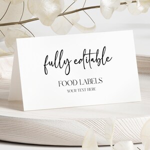 May include: A white, folded card with the words "fully editable" in elegant script, and "FOOD LABELS" below. The card sits on a light wooden tray, with decorative white leaves and branches in the background.