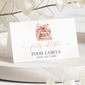 Può includere: Un biglietto bianco per etichette alimentari con un'illustrazione ad acquerello di una pila di libri legati con un fiocco rosa. Il biglietto recita "completamente modificabile" e "ETICHETTE ALIMENTARI IL TUO TESTO QUI" in elegante scrittura.