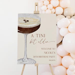 May include: A sign on a wooden easel with the text "A Tini bit older" and "Welcome to Nicole's 30th Birthday Party 06.22.XX". The sign features a watercolor illustration of a cocktail.