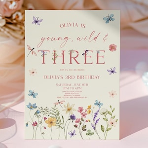 Peut inclure: Une invitation d'anniversaire avec le texte "Olivia is young, wild & THREE". L'invitation présente des illustrations florales et de papillons aux couleurs pastel. Les détails de l'événement incluent la date, l'heure et le lieu.
