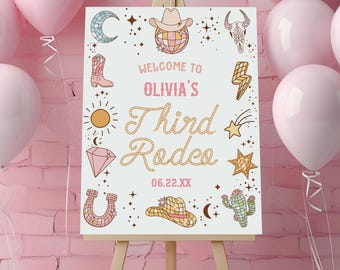 May include: A white rectangular sign on a wooden easel featuring the text Welcome to Olivia's Third Rodeo 06.22.XX. The sign is decorated with colorful illustrations of a disco ball cowboy hat, moon, boot, sun, diamond, horseshoe, cactus, and stars.