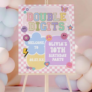 May include: A wooden easel displays a colorful sign with the words "Double Digits" in pastel colors. The sign welcomes guests to Olivia's 10th birthday party, featuring a checkered background and retro graphics like smiley faces and a peace sign.