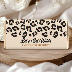 Könnte beinhalten: Rechteckige Schokoriegelverpackung mit beigem Hintergrund und Leopardenmuster. Der Text "Let's Get Wild!" und "EMILY'S 8TH BIRTHDAY" sind in Schwarz gedruckt. Der Schokoriegel liegt auf einem Holztablett.