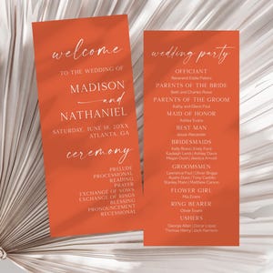 May include: Two rectangular orange wedding program cards with white text. The left card reads welcome to the wedding of Madison and Nathaniel, Saturday, June 18, 20XX, Atlanta, GA, and ceremony. The right card lists the wedding party and participants.