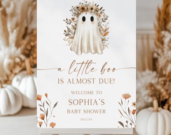 May include: A white rectangular sign on a wooden easel featuring a watercolor illustration of a ghost wearing a floral crown. The text reads: a little boo IS ALMOST DUE! WELCOME TO SOPHIA'S BABY SHOWER 09.22.XX, accented with orange floral stems.