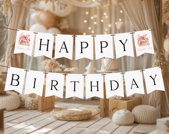 May include: A white banner with the words "HAPPY BIRTHDAY" in black capital letters. The banner is strung across a room decorated in neutral tones, including beige curtains, balloons, and wooden accents. The banner has illustrations of books with pink bows.