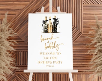 May include: A white sign with gold lettering announcing a "brunch & bubbly" birthday party for Taylor. The sign features a watercolor illustration of three champagne bottles with black and gold accents.