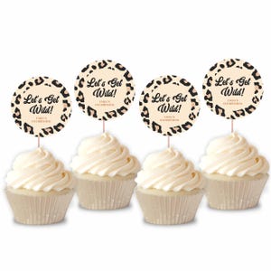 Pode incluir: Quatro cupcakes com cobertura branca e toppers decorativos. Os toppers são redondos com um design de estampa de leopardo e o texto "Let's Get Wild!" e "Emily's 4th Birthday".