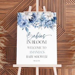May include: A white sign with blue floral decorations at the top. The sign reads "Babies in Bloom, Welcome to Amanda's Baby Shower, 08.22.XX".