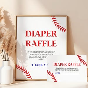 May include: A white sign with red text reading "DIAPER RAFFLE" in a gold frame. A smaller card with the same text and baseball-themed stitching is next to it. The sign is for a baby shower.