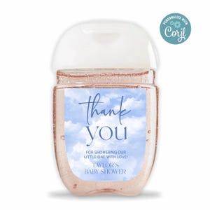 Puede incluir: Una pequeña botella de gel desinfectante de manos de plástico transparente con una tapa blanca y una etiqueta azul y blanca que dice "Gracias" con un fondo de cielo azul y nubes blancas. La etiqueta también dice "Por duchar a nuestro pequeño con amor! Baby Shower de Taylor".