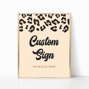 May include: A framed sign with a gold border features a cream-colored background. The top of the sign has a leopard print pattern. The words "Custom Sign" are written in black script, with "YOUR TEXT HERE" below in a smaller font.