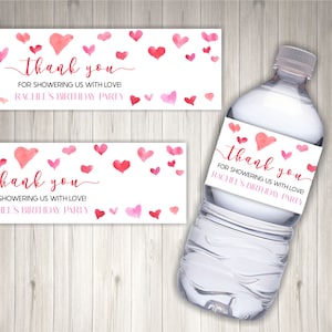 Peut inclure: Étiquette de bouteille d'eau avec des cœurs en aquarelle rose et le texte "merci de nous avoir comblé d'amour ! Anniversaire de Rachel".