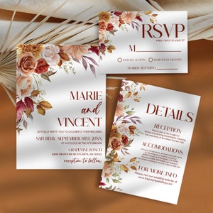 May include: Wedding invitation suite with a floral design featuring burgundy, peach, and cream flowers. The invitation includes the names Marie and Vincent, the wedding date, time, and location. The RSVP card includes the option to accept or decline the invitation and a space to indicate the number of guests attending. The details card includes information about the reception, accommodations, and a website for more information.