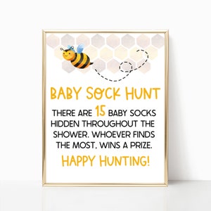 May include: A printable sign with a cartoon bee and honeycomb pattern. The sign says "Baby Sock Hunt" and "There are 15 baby socks hidden throughout the shower. Whoever finds the most, wins a prize. Happy Hunting!"