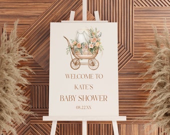 May include: A white sign with a gold baby carriage decorated with flowers. The sign reads "Welcome to Kate's Baby Shower 08.22.XX".