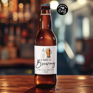 May include: A brown beer bottle with a white label that says "A Baby Is Brewing" with a baby bottle and a beer glass graphic. The label also includes the text "Kelly & Chris's Baby Shower 09.22.XXXX".