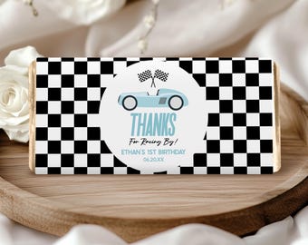 May include: A black and white checkered chocolate bar wrapper with a blue and white race car sticker. The sticker says "Thanks for Racing By! Ethan's 1st Birthday 06.20.XX"