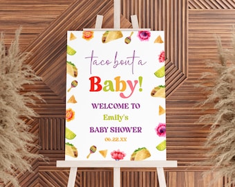 May include: A white sign with a colorful watercolor design featuring tacos, maracas, and flowers. The text on the sign reads "Taco Bout a Baby!" and "Welcome to Emily's Baby Shower 06.22.XX".