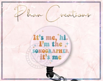 以下が含まれることがあります： ピンクの伸縮式バッジホルダーで、白い円の中に「It's me, hi. I'm the SONOGRAPHER it's me」というテキストが、カラフルなレトロなフォントで、金色の星と共に書かれています。