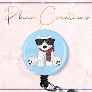 May include: A light blue retractable badge reel featuring a cartoon polar bear wearing sunglasses and a red and gray scarf. The badge reel has the text "Phan Creations" in gold script.