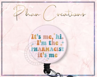May include: A light pink retractable badge reel with the text "It's me, hi. I'm the PHARMACIST it's me" in orange, teal, and brown. The reel has a black clip and a silver-colored metal clip.