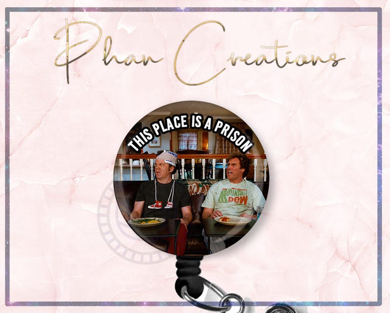 May include: A round retractable badge reel featuring a scene from a movie with two men seated at a table. The text "THIS PLACE IS A PRISON" is printed on the badge reel. The background is a pink marble design.