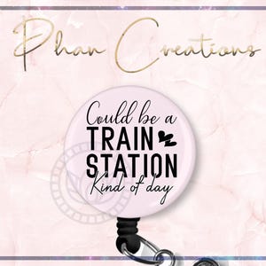 May include: White round badge with black text that reads "Could be a train station kind of day". The badge is attached to a black retractable badge reel.