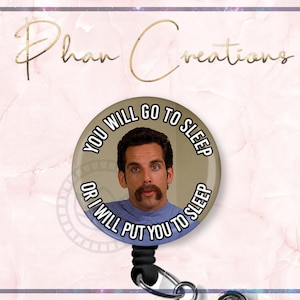 May include: A round, black and silver retractable badge reel with a circular design featuring a man with a mustache and the text "YOU WILL GO TO SLEEP OR I WILL PUT YOU TO SLEEP". The background is a light pink marble design.