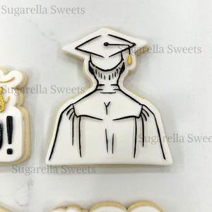 Könnte beinhalten: Ein weißer Keks, der mit schwarzem Zuckerguss verziert ist und eine Person darstellt, die von hinten eine Abschlusscap und eine Robe trägt. Der Keks ist ein Keks zum Thema Abschluss.