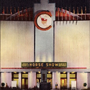 May include: A nighttime view of the entrance to the National Horse Show at the Coliseum, Canadian National Exhibition in Toronto, Canada. The building is lit up with lights and the sign above the entrance reads "HORSE SHOW".