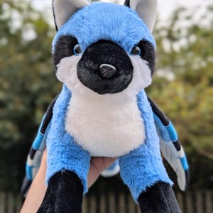May include: A plush blue jay stuffed animal with black and white accents. The bird has a white chest, black feet, and blue wings. The stuffed animal is soft and cuddly, perfect for a child's toy or a decorative item.