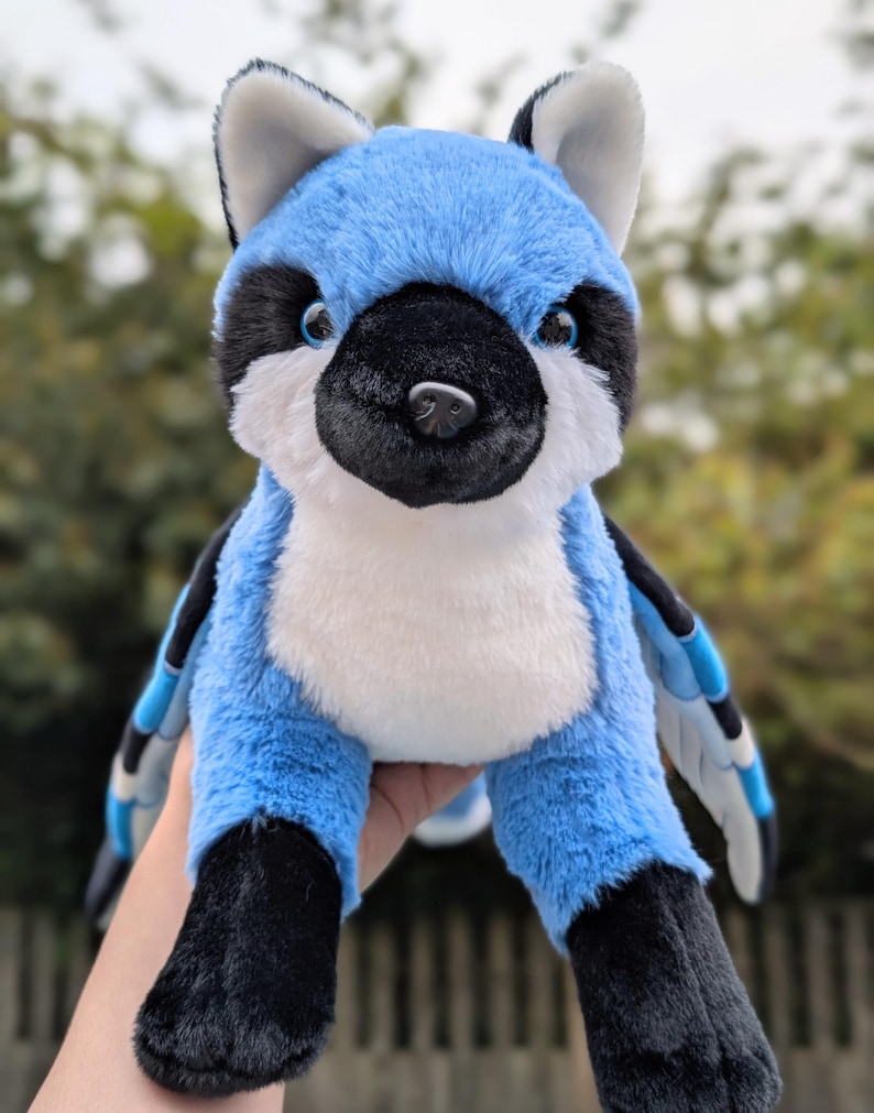 May include: A plush blue jay stuffed animal with black and white accents. The bird has a white chest, black feet, and blue wings. The stuffed animal is soft and cuddly, perfect for a child's toy or a decorative item.