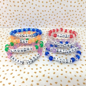 May include: Eight colorful beaded bracelets with words spelled out on them. The words are: Hydrate, Eat, Laundry, Brush Teeth, Study, Shower, Bathroom, and Dishes.