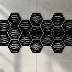 Könnte beinhalten: Schwarze geometrische Wandkunst, bestehend aus mehreren sechseckigen Formen. Jedes Sechseck weist ein gepunktetes Muster auf, das einen strukturierten Effekt erzeugt. Die Anordnung ist an einer hellgrauen Wand montiert, wobei Schatten Tiefe verleihen.