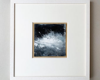 May include: A framed abstract painting with a white burst of color on a black background.