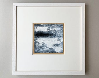 May include: A framed abstract painting with a white mat and a white frame. The painting is a mix of white, gray, and black paint, creating a textured and layered effect.