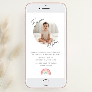Könnte beinhalten: Eine digitale Einladung zu einer zweiten Geburtstagsfeier für ein Kind. Die Einladung zeigt ein Foto eines Kindes in einem weißen Shirt, eine Regenbogengrafik und den Text "Emma ist zwei!" Bitte schließen Sie sich uns an, um am Samstag, den 18. August um 14:00 Uhr zu feiern 100 Willow Av Bridgeton, TD4 5678 Bitte melden Sie sich bei Sarah 07888 888888